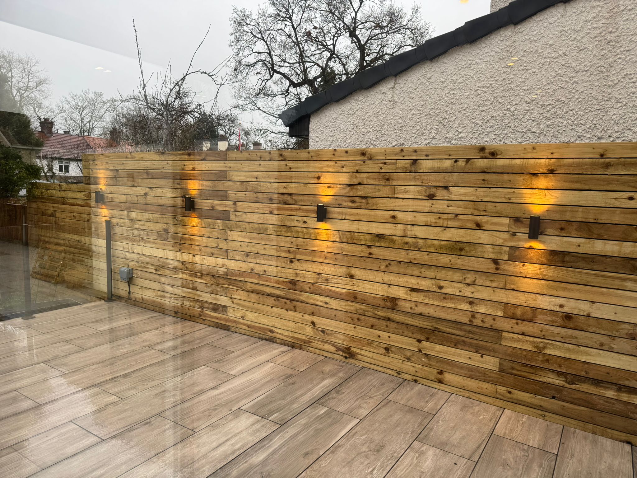 Warm garden wall lights fitted along a timber fence